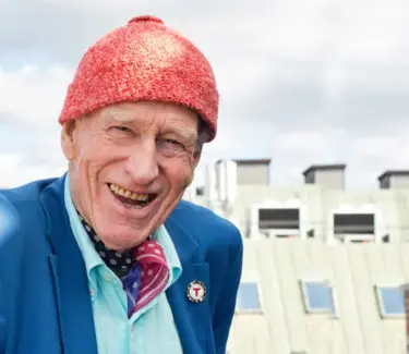 Nærbilde av Olav Thon, med signatur-luen, med en fin utsikt av Oslo bak