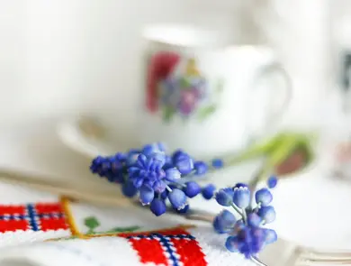 Blå perleblomster på et bord med duk med broderier av det norske flagget. Foto til artikkel om borddekking til 17. mai