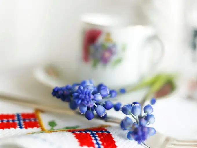 Blå perleblomster på et bord med duk med broderier av det norske flagget. Foto til artikkel om borddekking til 17. mai