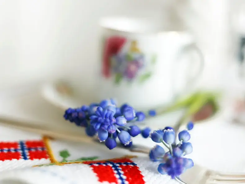 Blå perleblomster på et bord med duk med broderier av det norske flagget. Foto til artikkel om borddekking til 17. mai