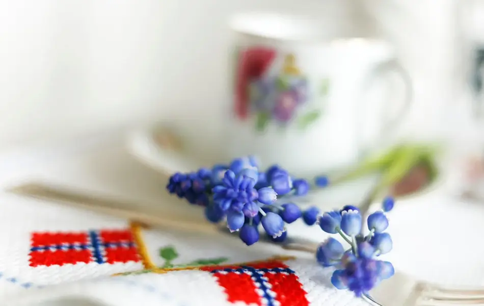 Blå perleblomster på et bord med duk med broderier av det norske flagget. Foto til artikkel om borddekking til 17. mai