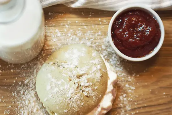 En bolle med krem, et beger jordbærsyltetøy og et glass melk står på et bord