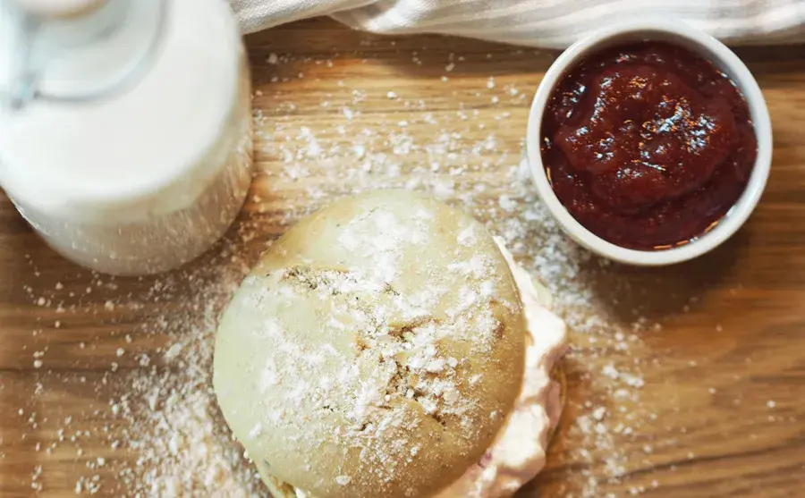En bolle med krem, et beger jordbærsyltetøy og et glass melk står på et bord