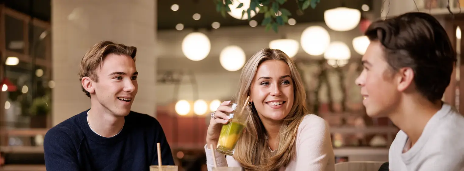 To gutter og en jente som sitter ved et bord i en kafé med drikke og mat på bordet