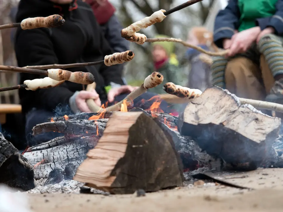 Family grilling bread on a stick over an open fire
