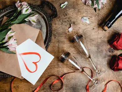 Blomster, to vinglass, kort med hjerte på og flaske på et bord