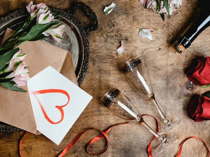 Blomster, to vinglass, kort med hjerte på og flaske på et bord