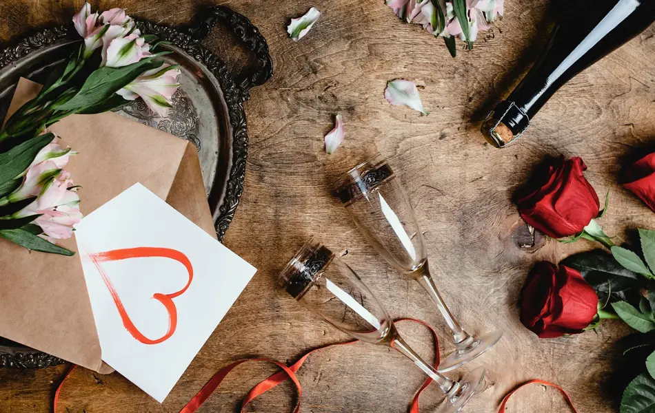 Blomster, to vinglass, kort med hjerte på og flaske på et bord