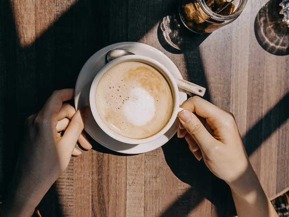 Top view of woman sitting by the window in coffee shop enjoying the warmth of sunlight and drinking coffee