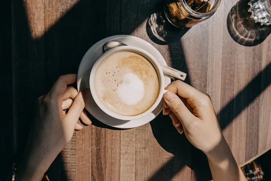 Top view of woman sitting by the window in coffee shop enjoying the warmth of sunlight and drinking coffee