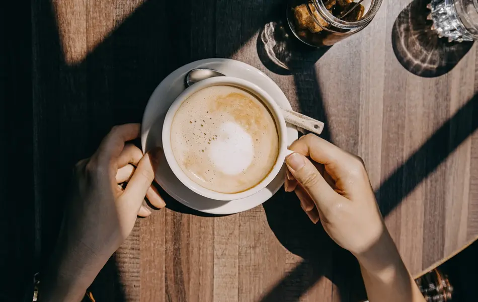 Top view of woman sitting by the window in coffee shop enjoying the warmth of sunlight and drinking coffee