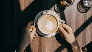 Top view of woman sitting by the window in coffee shop enjoying the warmth of sunlight and drinking coffee