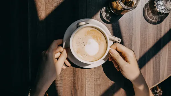 Top view of woman sitting by the window in coffee shop enjoying the warmth of sunlight and drinking coffee