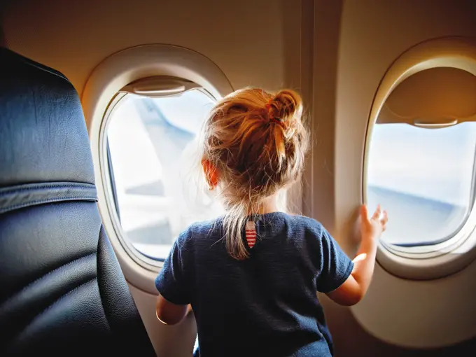 Adorable little girl traveling by an airplane. Child sitting by aircraft window and looking outside. Traveling with kids abroad. Family on summer vacations.