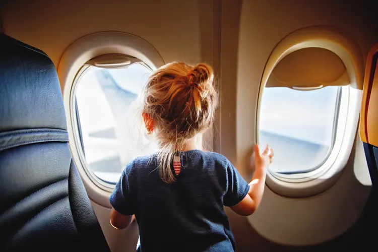 Adorable little girl traveling by an airplane. Child sitting by aircraft window and looking outside. Traveling with kids abroad. Family on summer vacations.