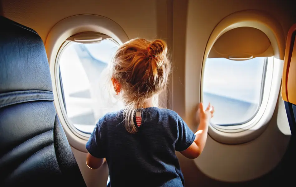 Adorable little girl traveling by an airplane. Child sitting by aircraft window and looking outside. Traveling with kids abroad. Family on summer vacations.