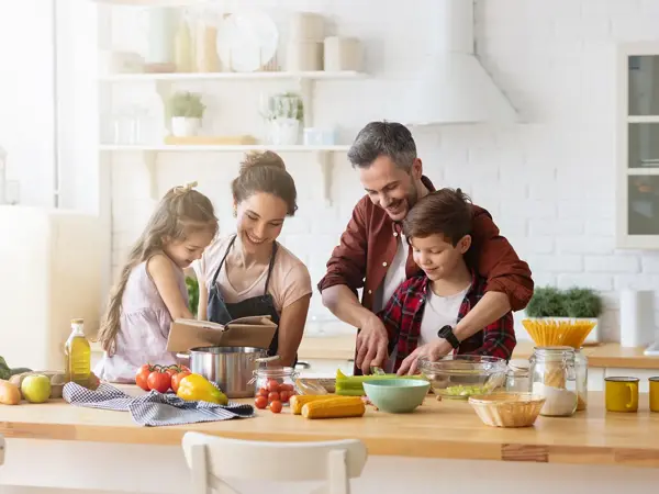 Totalbilde. Mann, dame og to barn lager mat på lyst kjøkken. Foto til artikkel om gaver til pappatyper på farsdag.