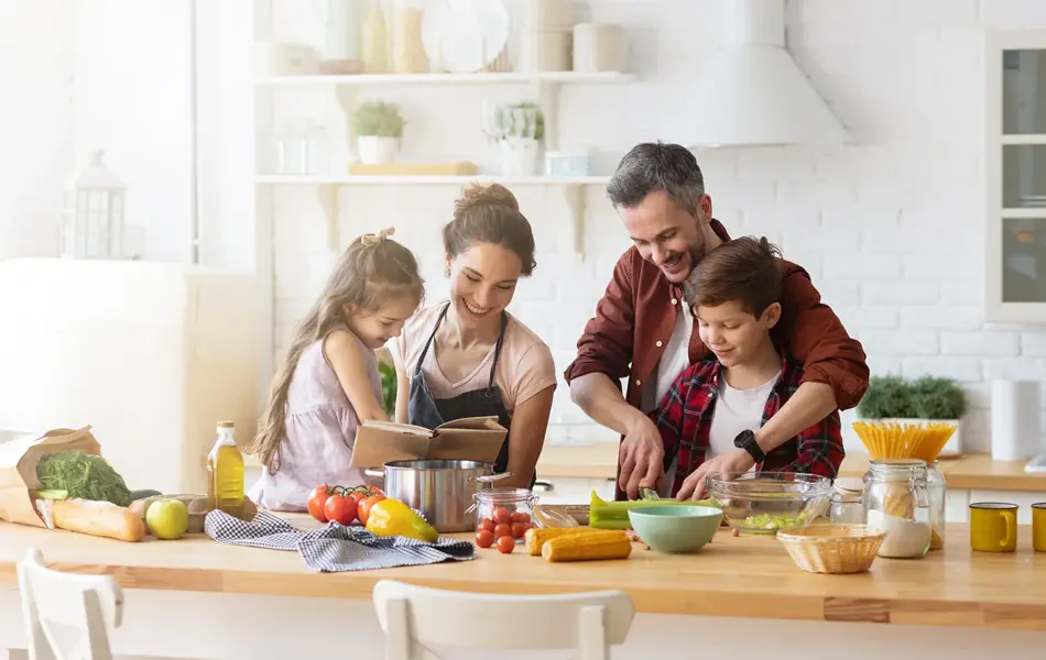Totalbilde. Mann, dame og to barn lager mat på lyst kjøkken. Foto til artikkel om gaver til pappatyper på farsdag.