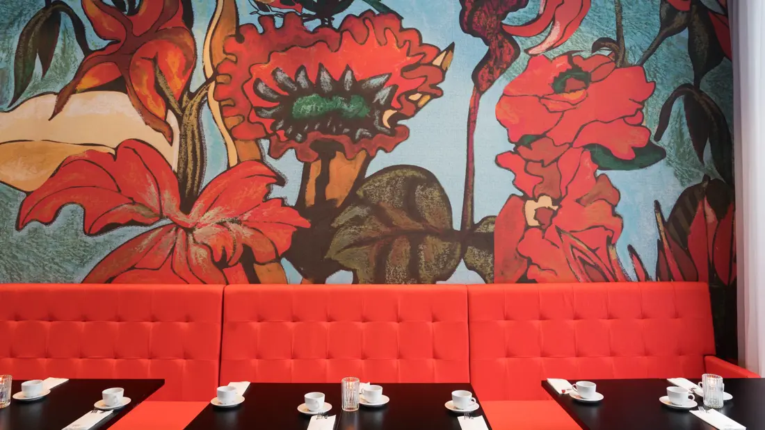 Knall rød sofa med røde store blomster på tapet i bagrunnen i restaurant på Thon Hotel Kirkenes ved kaia i Kirkenes sentrum