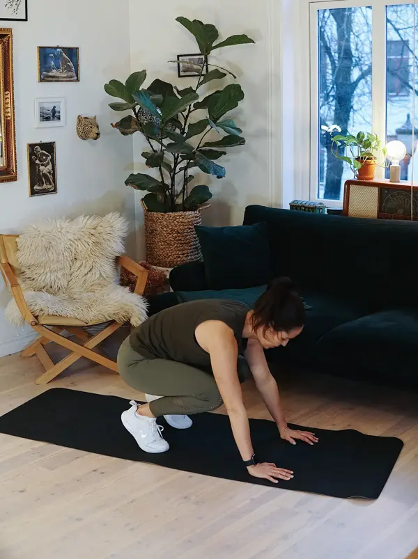 treningsekspert Anna Johansen trener på matte på gulvet, mørkegrønn sofa i bakgrunnen, lys stol med pels oppi, str grønn plante, bilder på veggen
