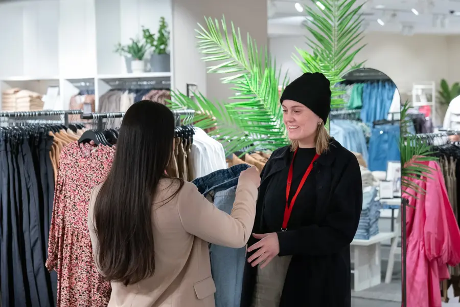 To jenter som snakker sammen inne i en butikk, ser på en bukse 