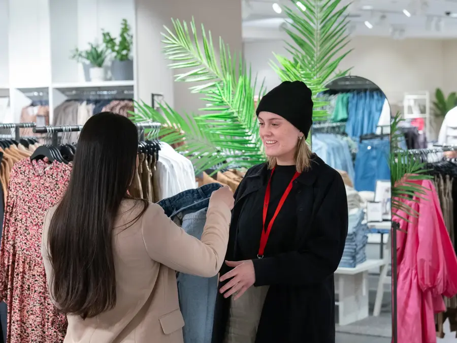 To jenter som snakker sammen inne i en butikk, ser på en bukse 