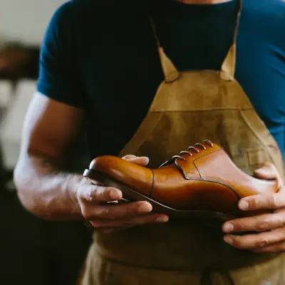 mann i mørk tskjorte iført forkle holder en brun skinnsko