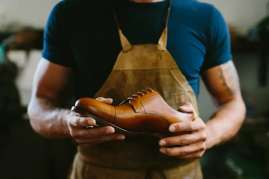 mann i mørk tskjorte iført forkle holder en brun skinnsko