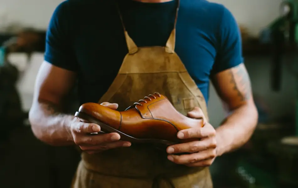 mann i mørk tskjorte iført forkle holder en brun skinnsko