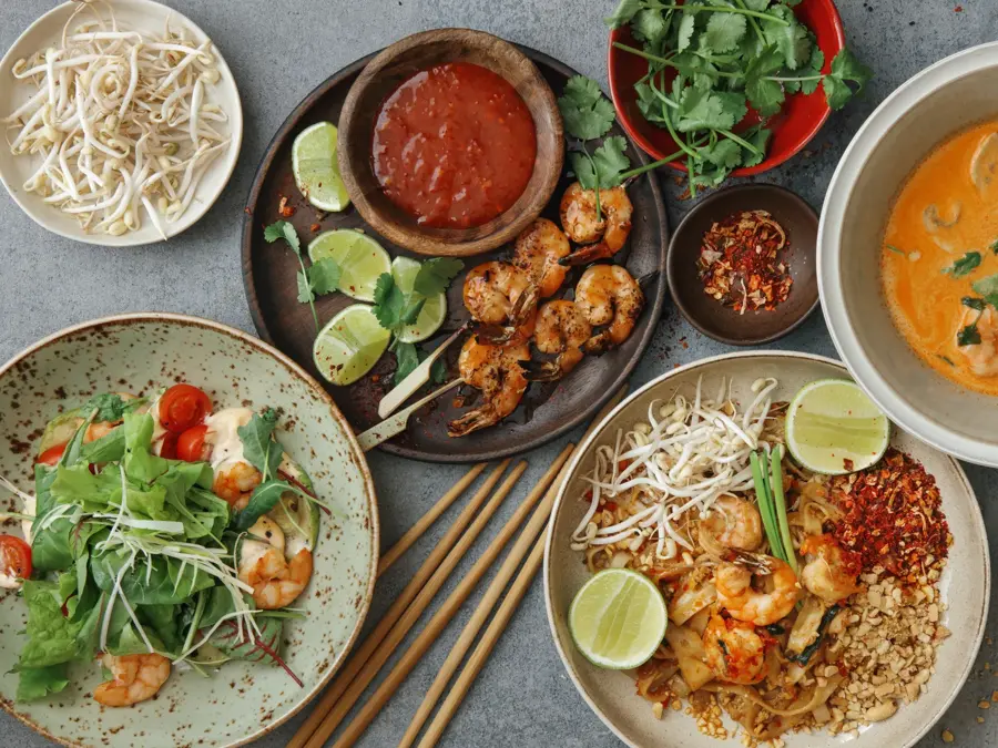 Authentic classic Pad Thai with shrimps. Thai shrimp satay with sweet chili sauce. Tom Yum soup with coconut milk (Tom Khaa). Spicy shrimp salad. Flat lay top-down composition on concrete background.