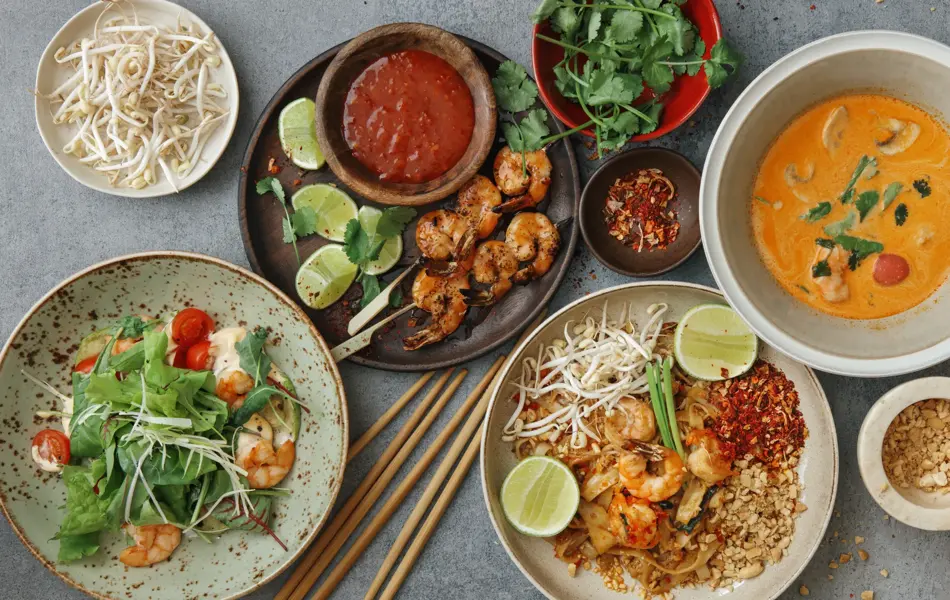 Authentic classic Pad Thai with shrimps. Thai shrimp satay with sweet chili sauce. Tom Yum soup with coconut milk (Tom Khaa). Spicy shrimp salad. Flat lay top-down composition on concrete background.