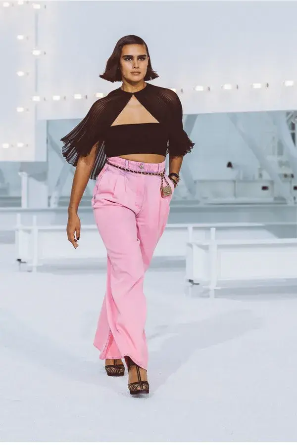 Dame som går på catwalk med rosa bukse , sort liten tubetopp og et tynt belte.