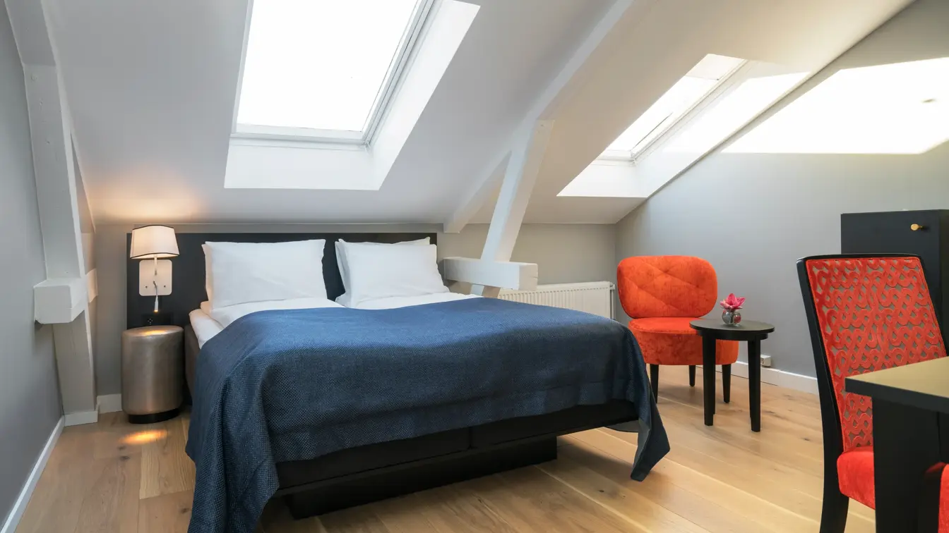 Dobbeltseng med orange stol og skråtak i standard double room på Thon Hotel Spectrum i Oslo sentrum