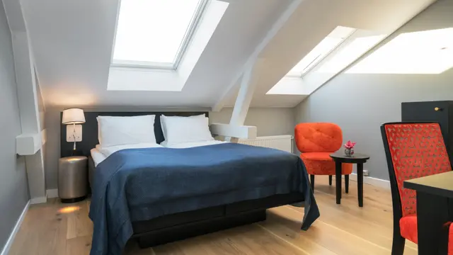 Dobbeltseng med orange stol og skråtak i standard double room på Thon Hotel Spectrum i Oslo sentrum