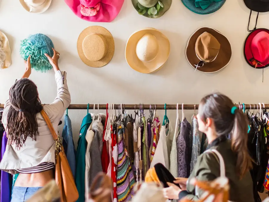 To unge kvinner prøver hatter i en butikk med vintageklær.