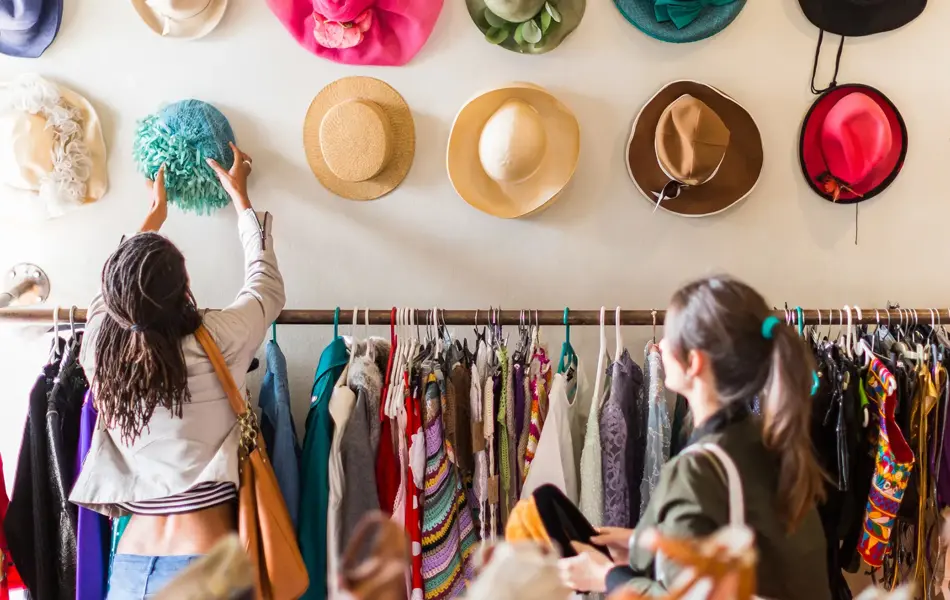 To unge kvinner prøver hatter i en butikk med vintageklær.
