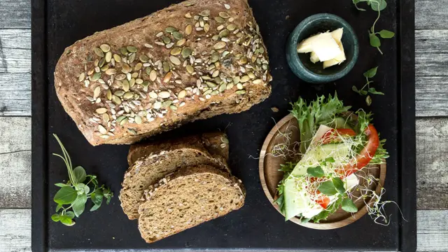 Miljøbilde med surdeigsbrød, to brødskiver og pålegg på en fjøl