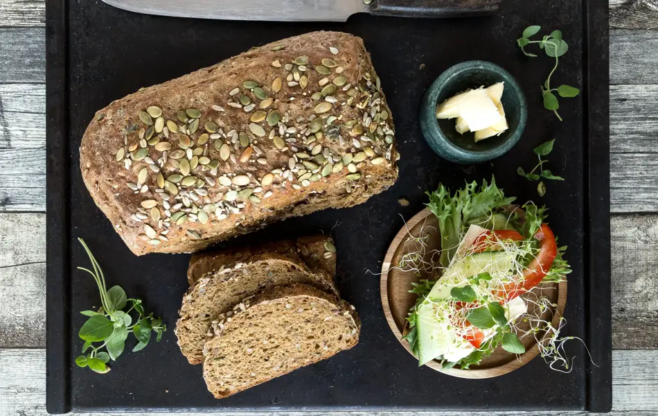 Miljøbilde med surdeigsbrød, to brødskiver og pålegg på en fjøl