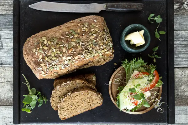 Miljøbilde med surdeigsbrød, to brødskiver og pålegg på en fjøl