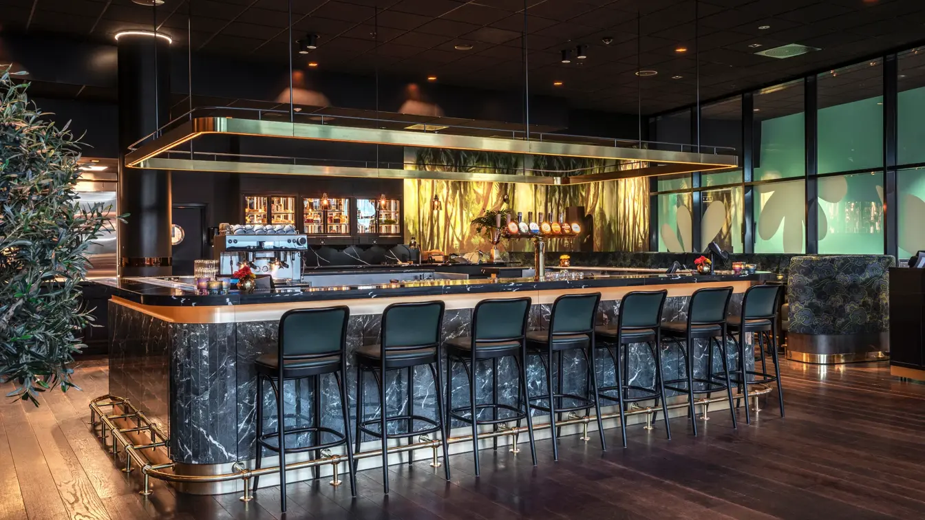 Baren hos Thon Hotel Storo. Mørk bardisk med tilhørende mørke barstoler. Mørkt parkettgulv.