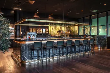 Baren hos Thon Hotel Storo. Mørk bardisk med tilhørende mørke barstoler. Mørkt parkettgulv.