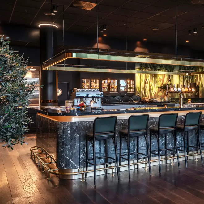 Baren hos Thon Hotel Storo. Mørk bardisk med tilhørende mørke barstoler. Mørkt parkettgulv.