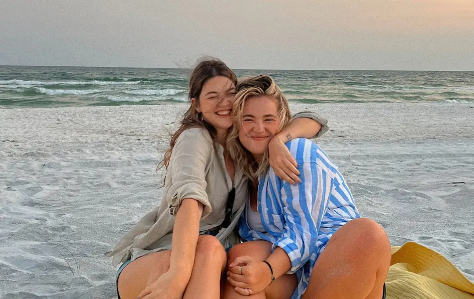 To damer som klemmer hverandre og sitter på en strand