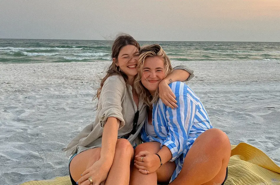 To damer som klemmer hverandre og sitter på en strand