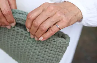 To hender med en diamantring holder en heklet grønn veske.