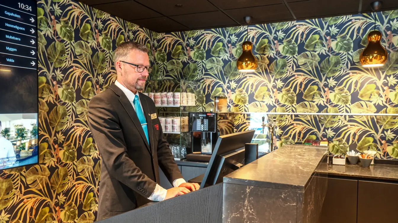 Resepsjonist står bak resepsjonsdesk.