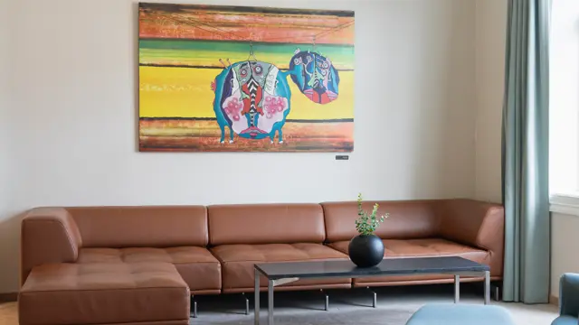 Stor brun skinnsofa på suite med sofabord og fargerikt bilde på veggen