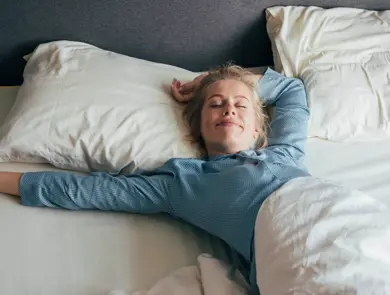 Dame som ligger i sengen og smiler med lukkede øyne