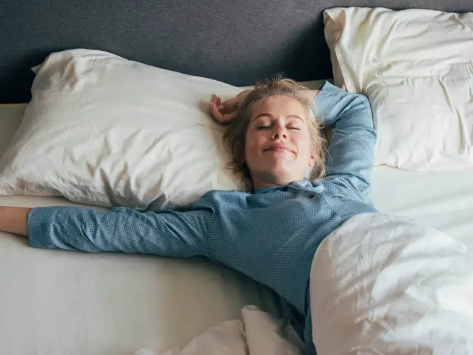 Dame som ligger i sengen og smiler med lukkede øyne