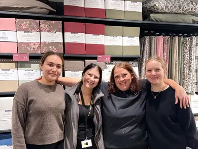 tre mørkhårete og ei lyshåret jente står foran mange fargerike gardinpakker